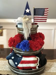 patriotic tiered tray decor with USA flag, Uncle Sam themed gnome, candles, USA themed bull, and faux red, white, and blue flowers