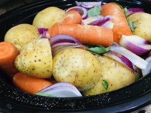 crockpot full of ingredients for dinner, including potatoes, carrots, and onions