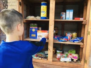 Photo of young boy stocking a small outdoor food pantry.