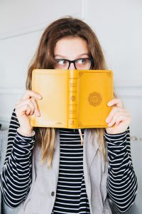 woman holding a bible in front of her face and peeking her eyes out from the top
