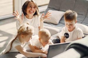 Frustrated Mom on the floor with her kids, who are distracted by a computer