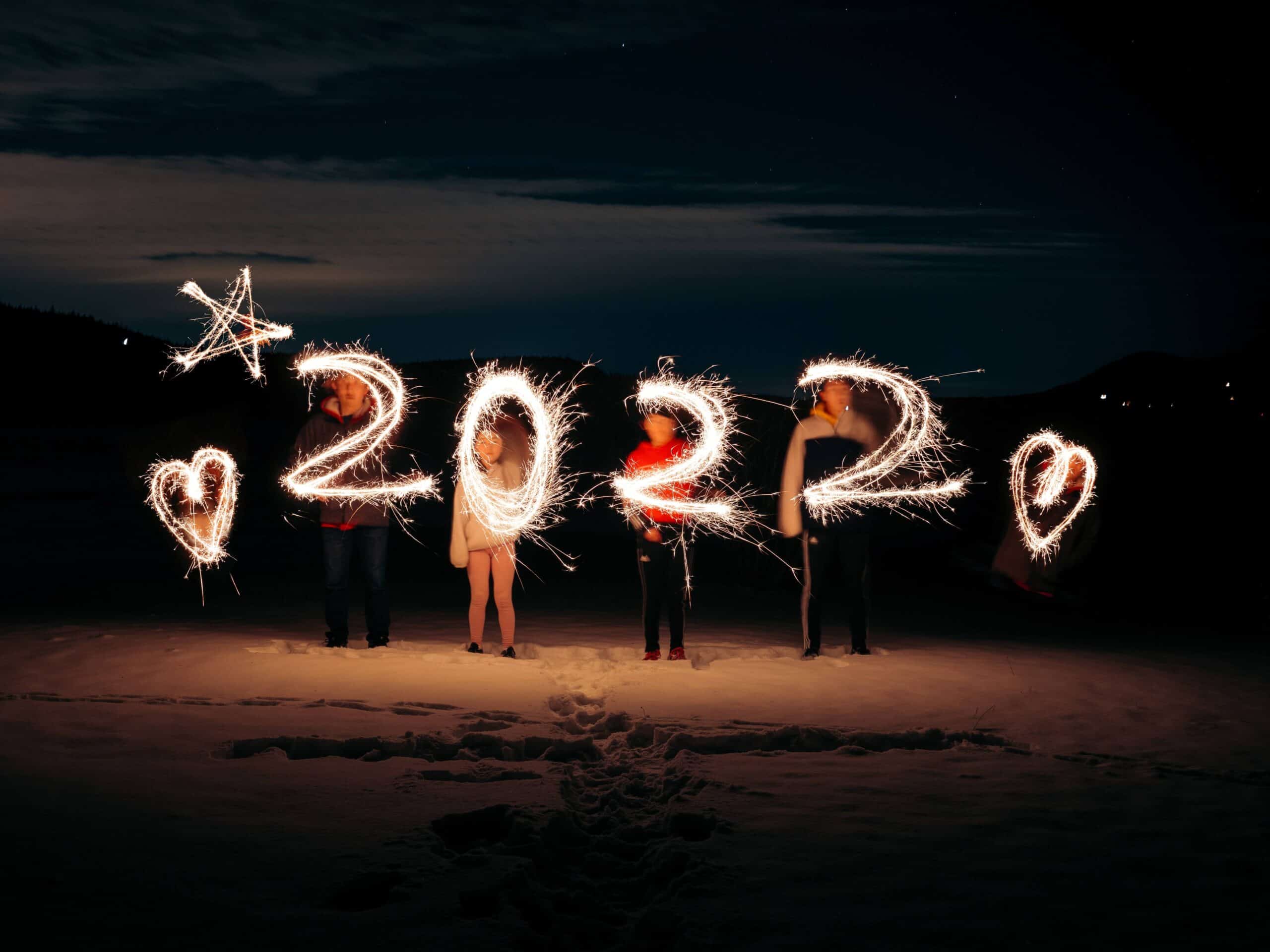 4 people on a beach at dark writing 2022 in the air with sparklers