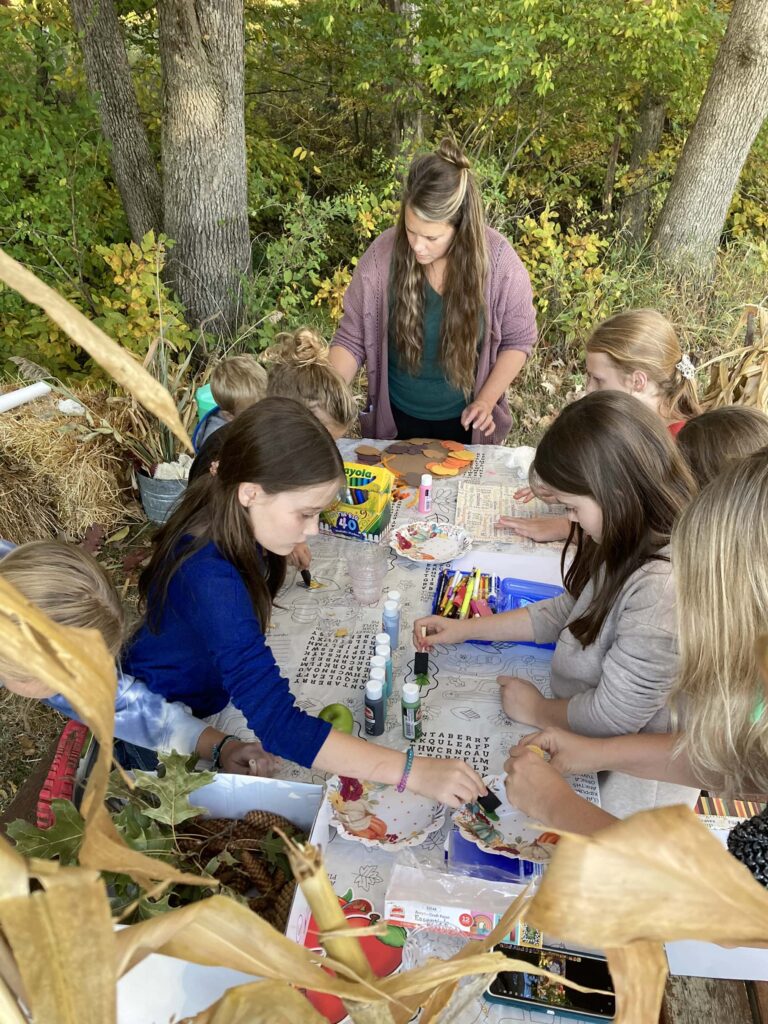 As crianças sentam-se à mesa do lado de fora e fazem projetos de arte para celebrar a Festa dos Tabernáculos