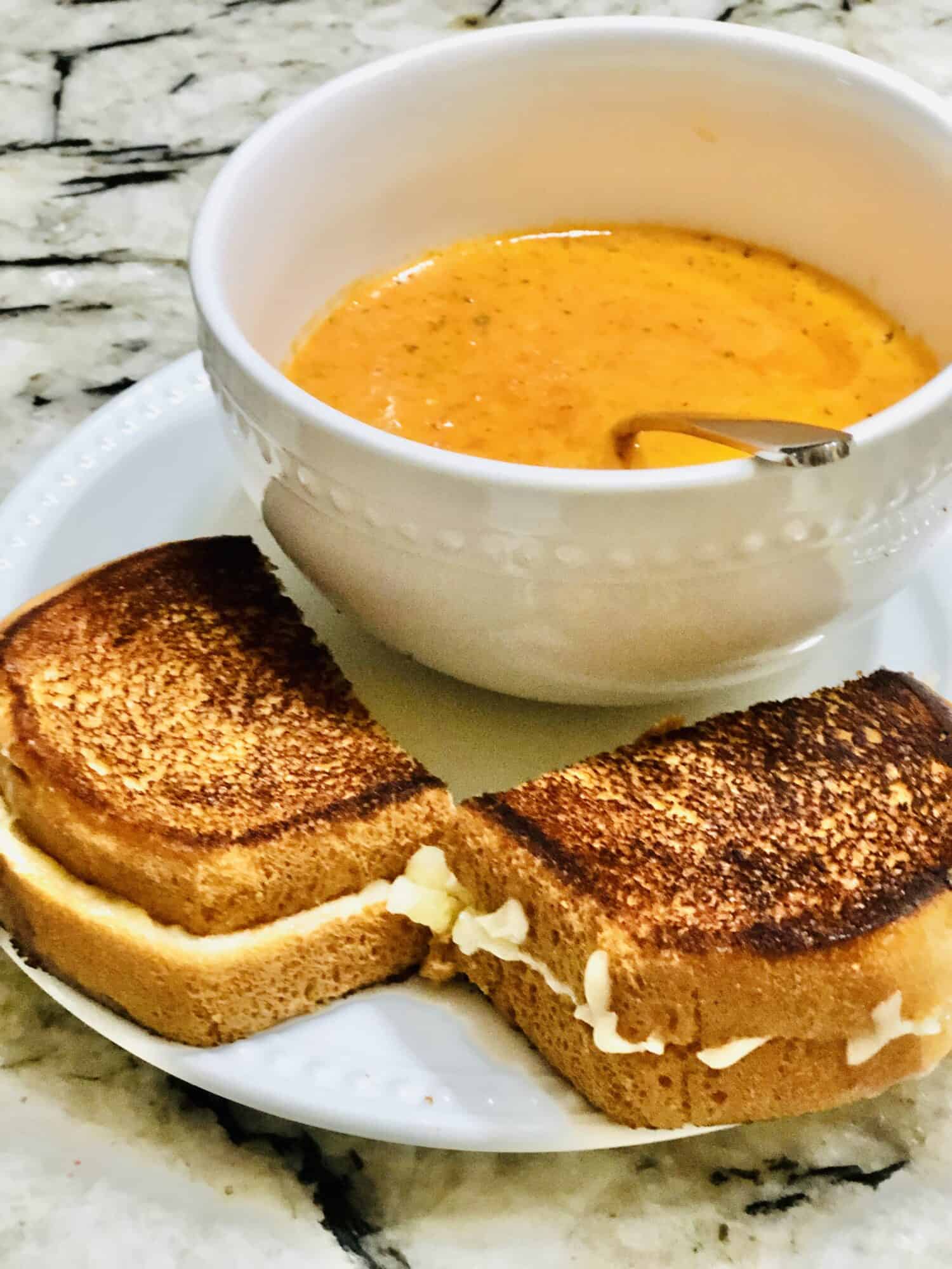 Spicy Creamy Tomato Soup in a bowl with a side of grilled cheese