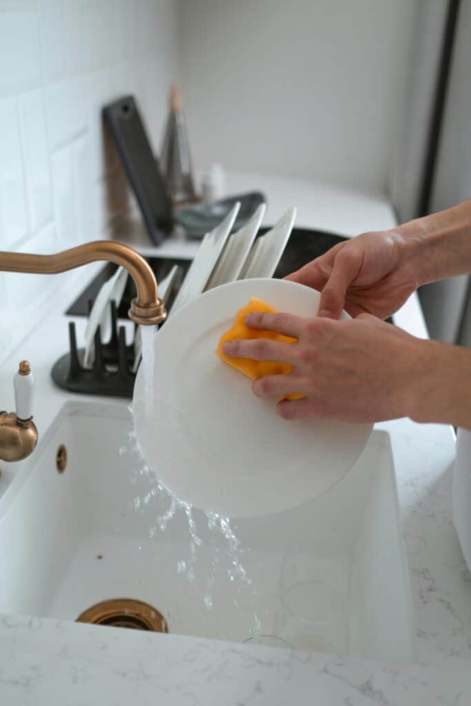 morning cleaning routine: person washing white plate with a sponge