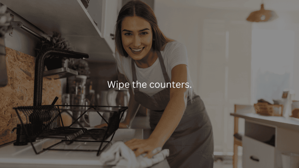 Nightly cleaning routine: wipe the counters. Woman looking at the camera and smiling while wiping kitchen counters. 